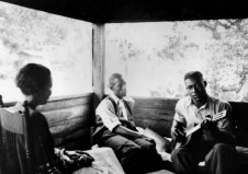 Gabriel Brown playing guitar as Rochelle French and Zora Neale Hurston listen